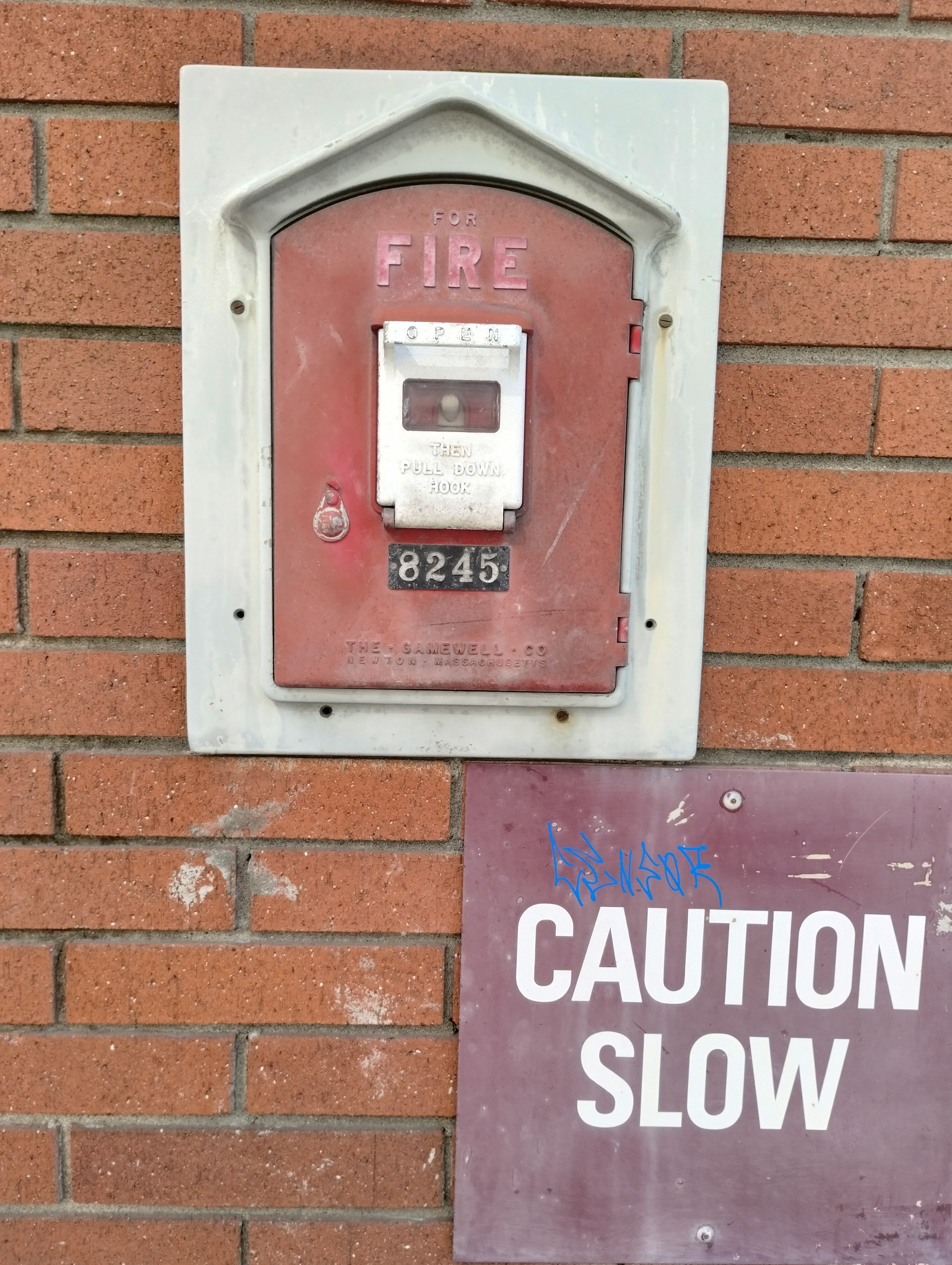 a publicly exposed fire alarm pull tab on a brick wall. below and to the right is a different sign that reads, CAUTION SLOW in large bold font